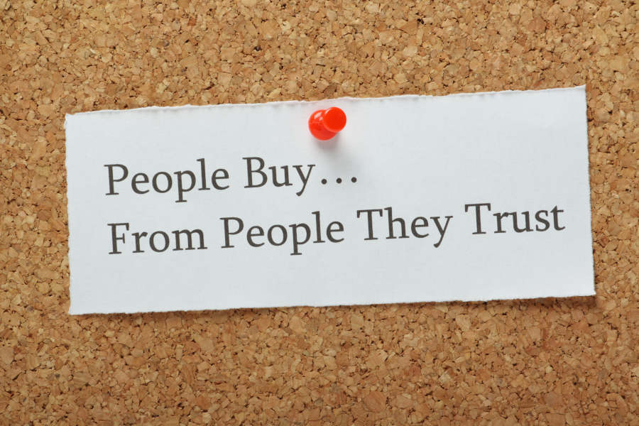 Image of a corkboard with a piece of paper that says, “people buy from people they trust”.