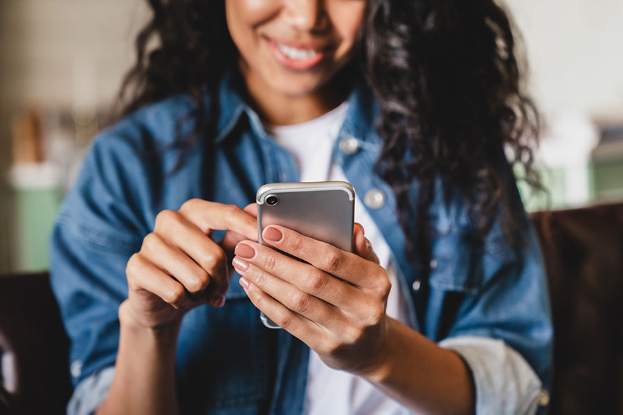 A woman wearing a jean jacket and smiling while using a mobile responsive website on her smartphone in Rockledge, FL.