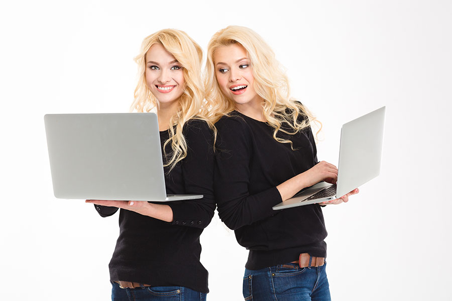 Identical blonde twin girls with two identical grey laptops browsing the internet in Titusville, FL.