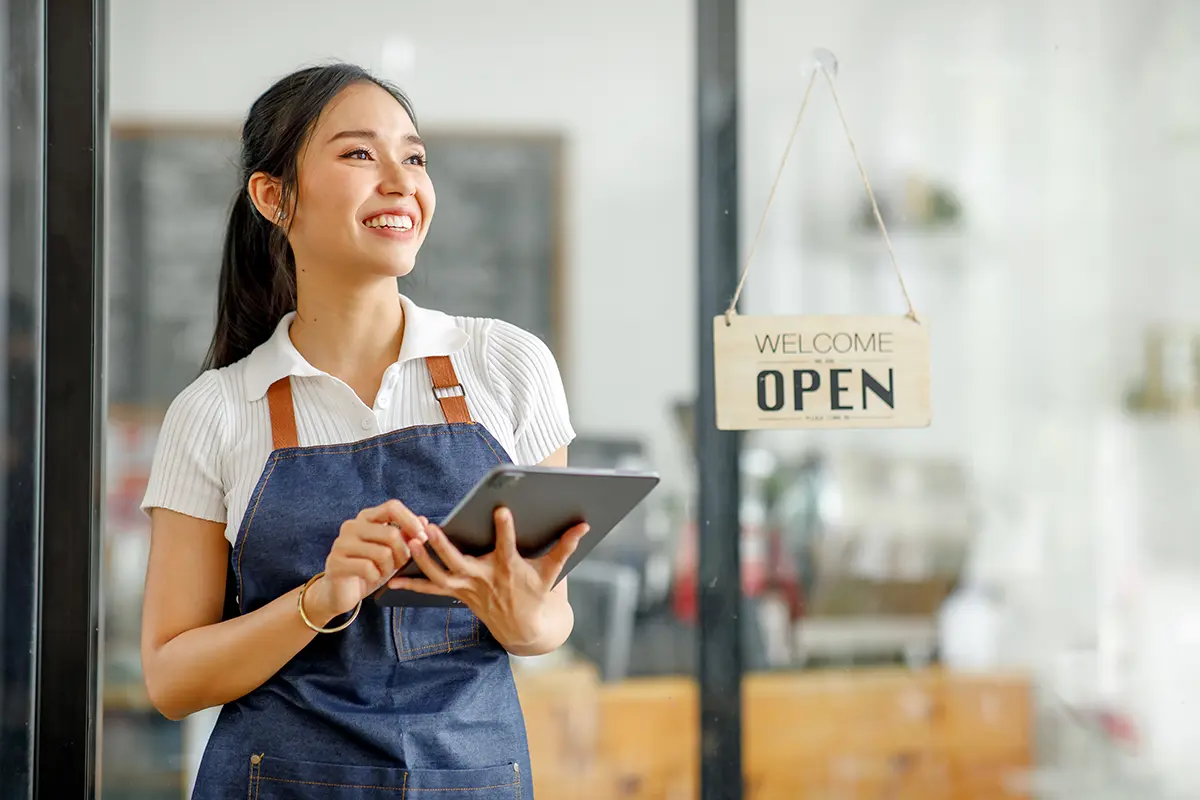 Young businesswoman small business owner standing at cafeteria door entrance pen signboard