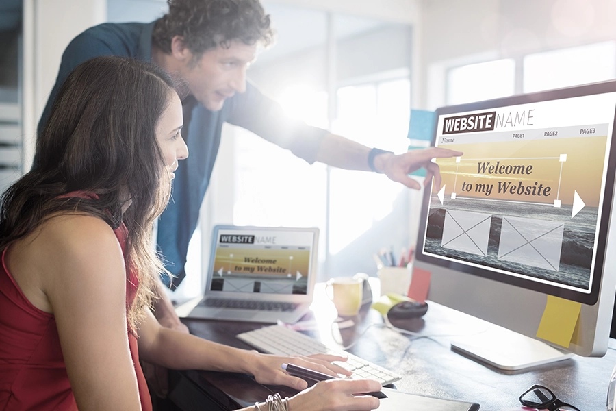 A man and a woman working together to build a website on a computer in an office space for a St. Louis business.