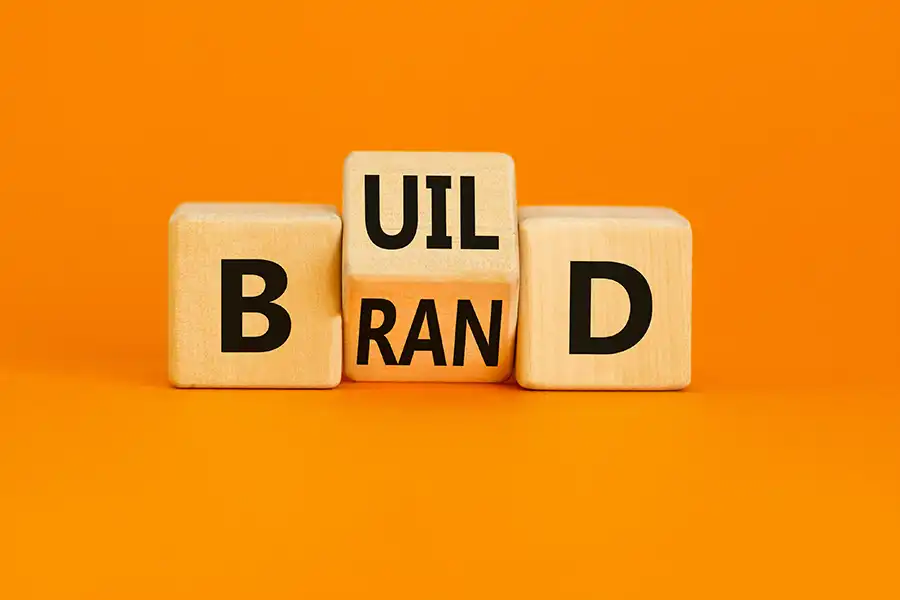 Right Click Digital, Inc. – Wooden letter blocks arranged on an orange background spell “BUILD” above “BRAND,” symbolizing the concept of building a strong brand identity.
