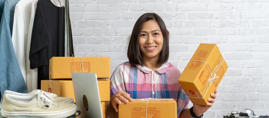 Businesswoman with sealed boxes and laptop on a wooden desk packaging custom clothing items